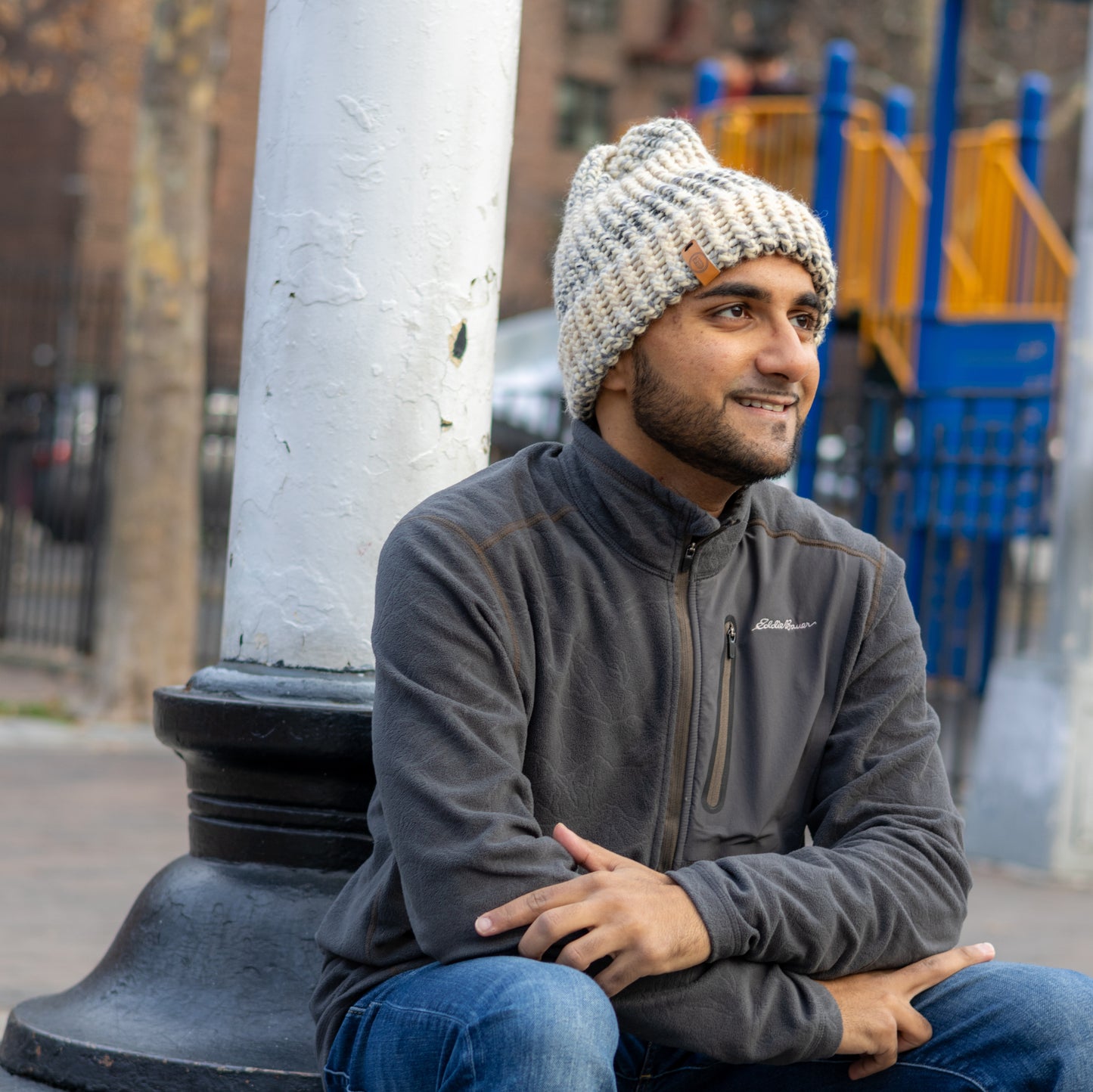 Man wearing a Handmade Cream & Gray Knit Beanie, smiling while seated outdoors on a bench in a park