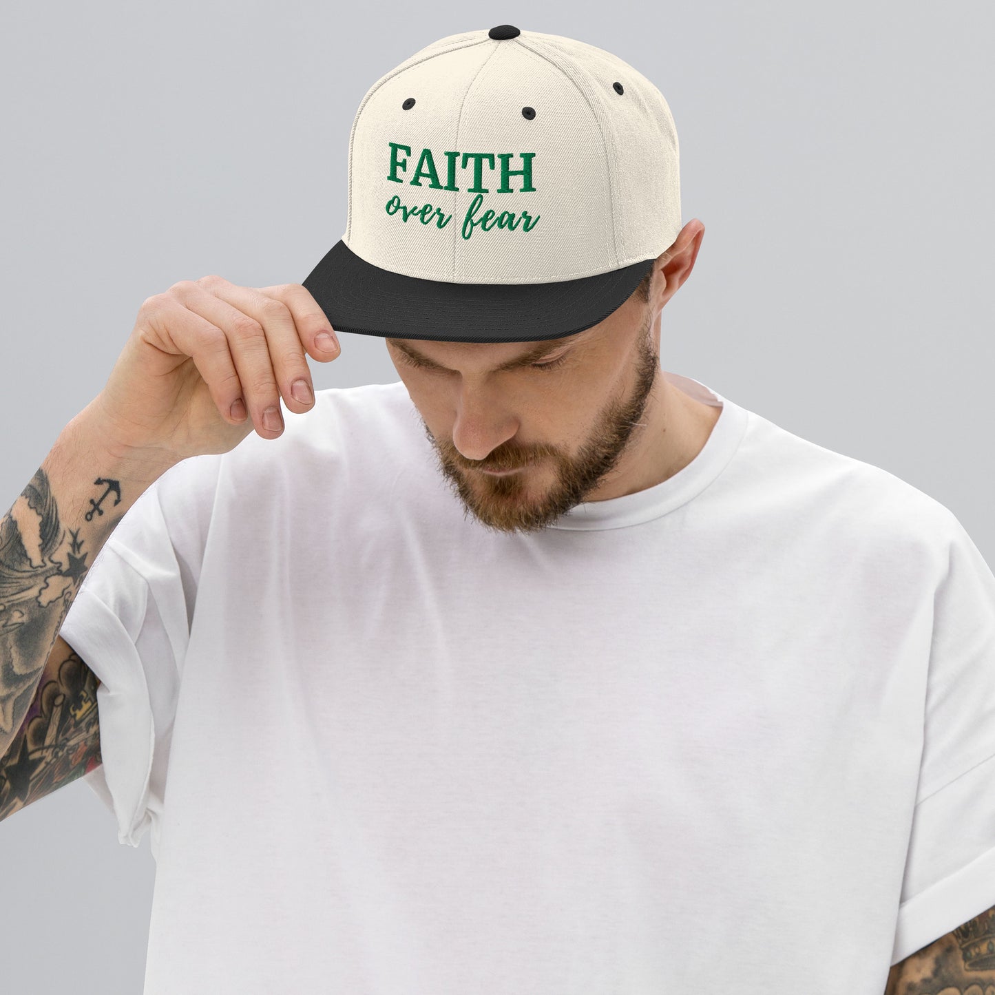 Beige FAITH OVER FEAR – Embroidered Snapback Hat with green embroidery, styled on male model in white shirt