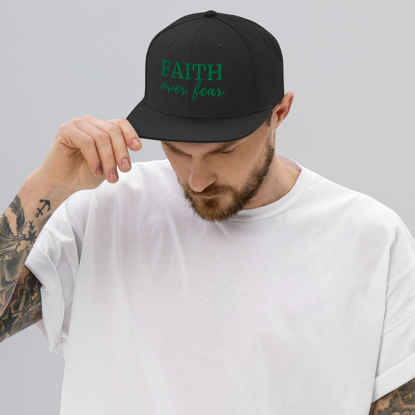Black FAITH Over Fear embroidered snapback hat with green thread, worn by male model