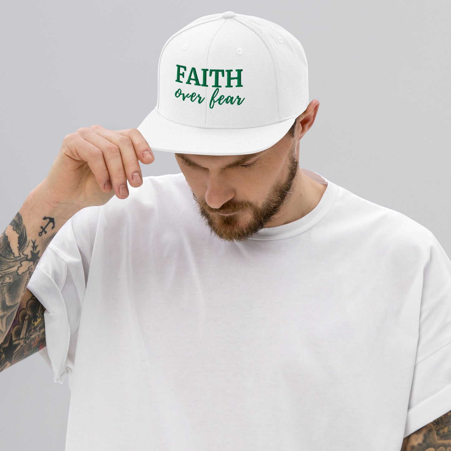 White FAITH Over Fear hat with green stitched lettering, worn casually by male model