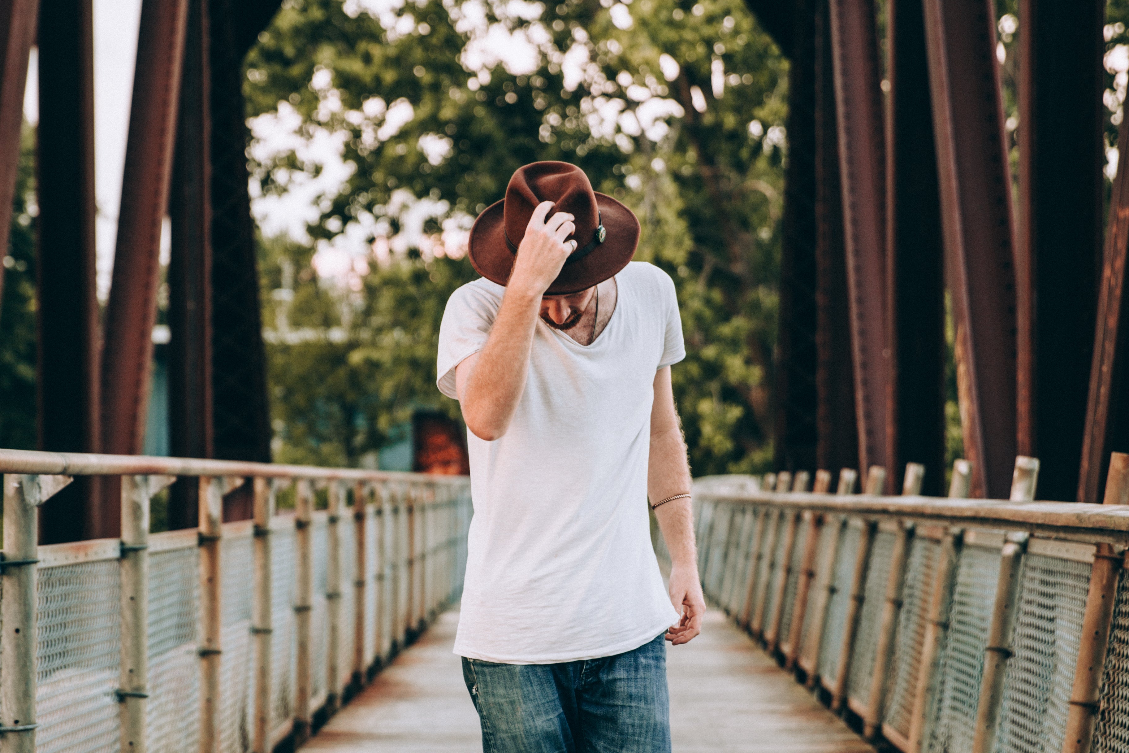 MENS FASHION WALKING ACROSS BRIDGE HOLDING HAT