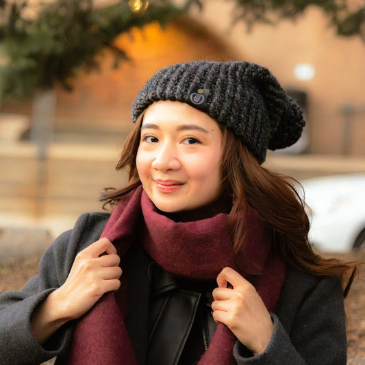 Woman wearing a handmade charcoal slouchy crochet beanie and burgundy scarf, smiling outdoors in a gray coat during winter.