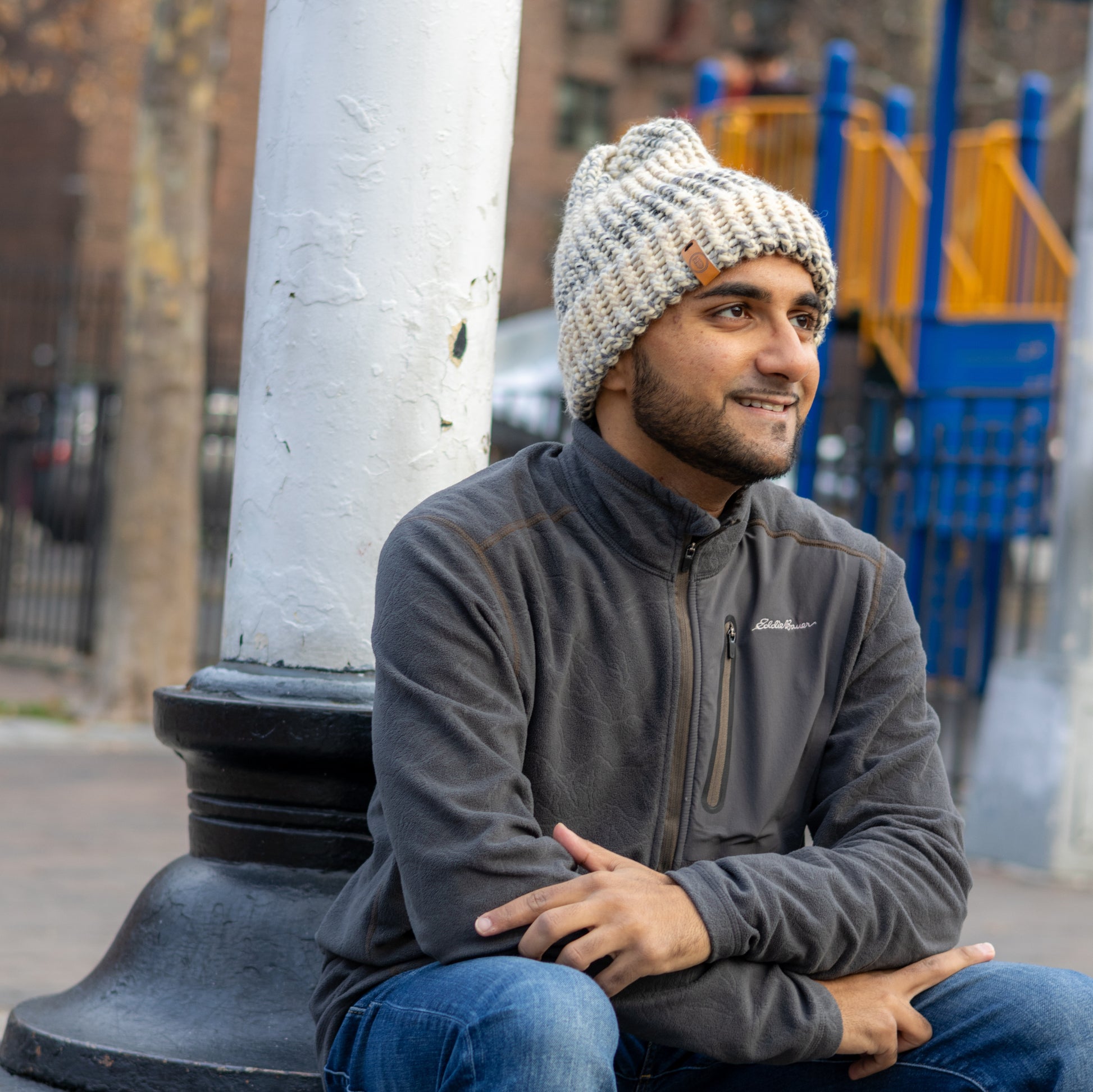 Man wearing a Handmade Cream & Gray Knit Beanie, smiling while seated outdoors on a bench in a park