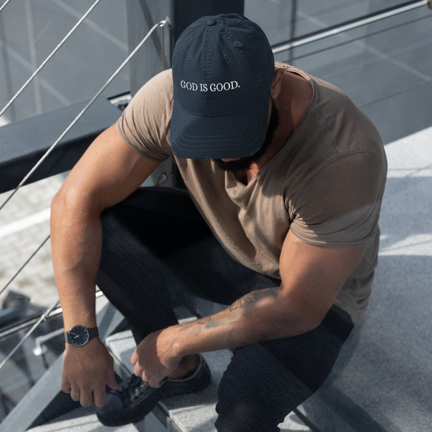 Side angle of navy GOD IS GOOD Christian dad hat worn by model sitting on stairs