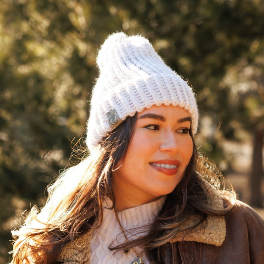 Woman wearing a handmade ivory white knit beanie and shearling jacket, smiling in the sunlight outdoors.