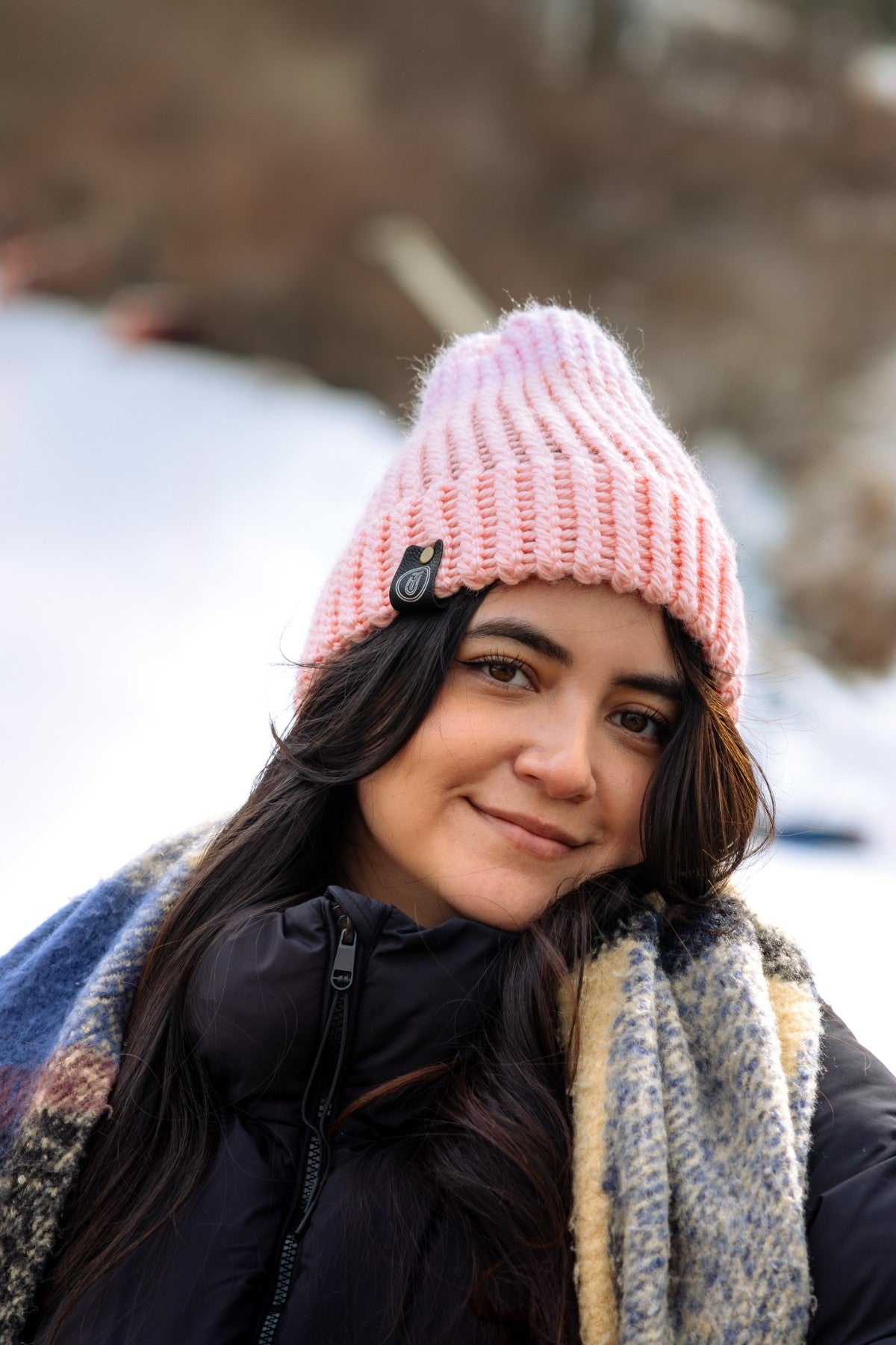 Woman in a peach-colored crochet beanie and wool scarf, smiling in the snow with soft winter light.