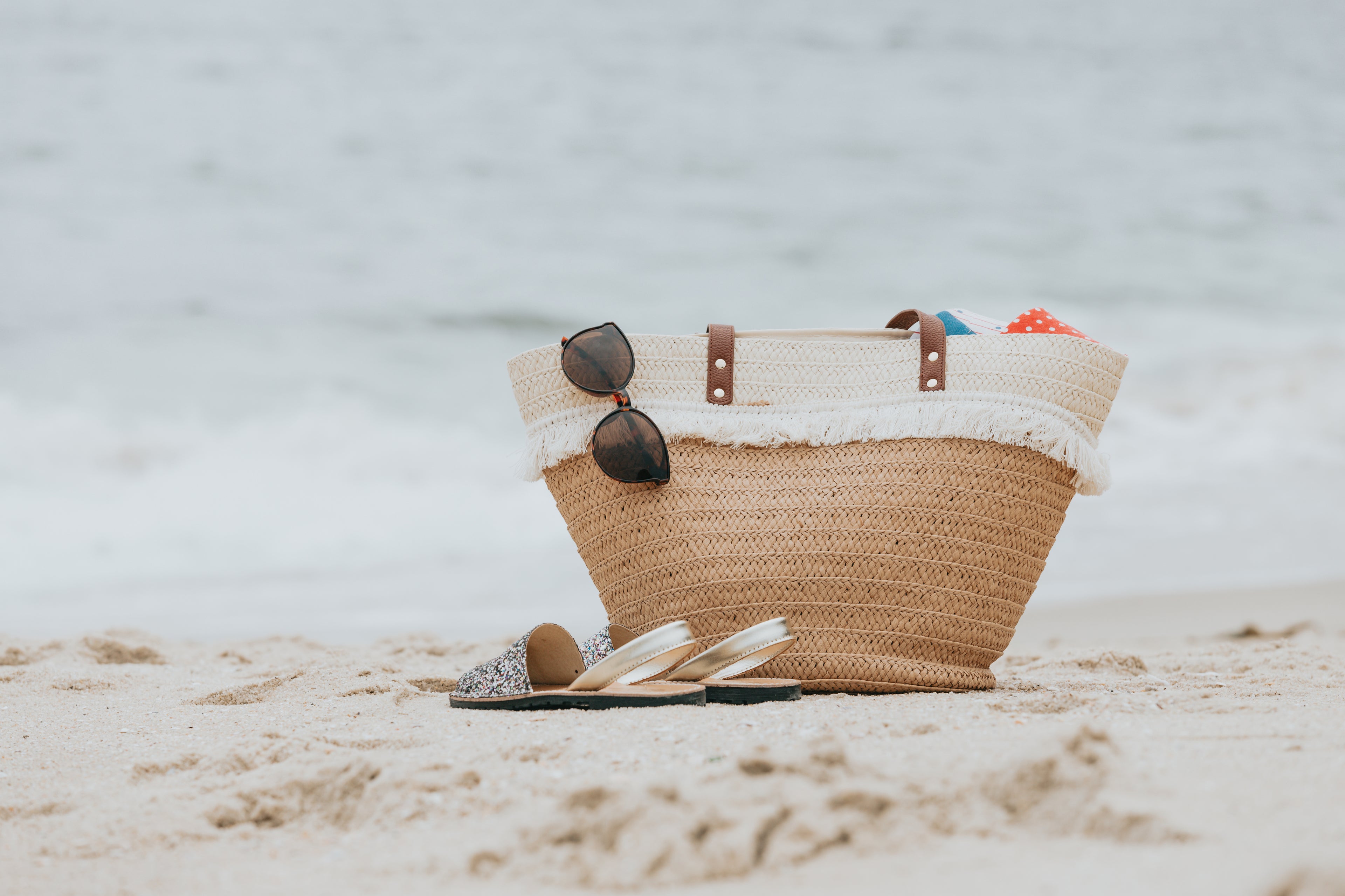 Beachbag, sunglass, and flip flops on beach shoreline