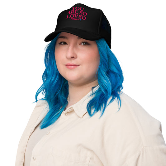Woman wearing black Christian YOU ARE SO LOVED Trucker Hat with pink embroidery and light blue cross