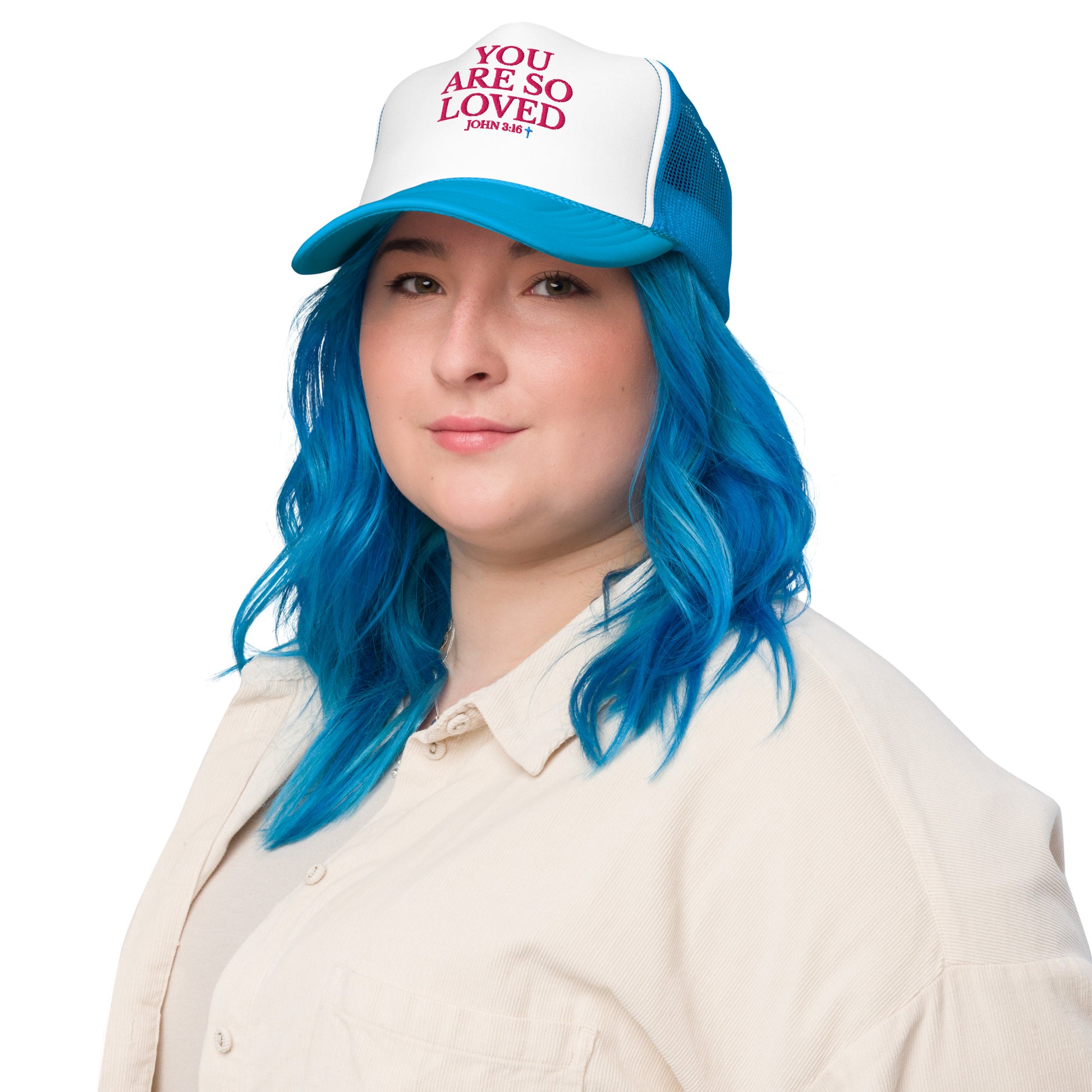 Model with blue hair wearing white and blue YOU ARE SO LOVED Christian trucker hat with bold pink lettering